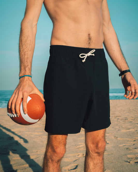 Man in black shorts holding a football on a beach