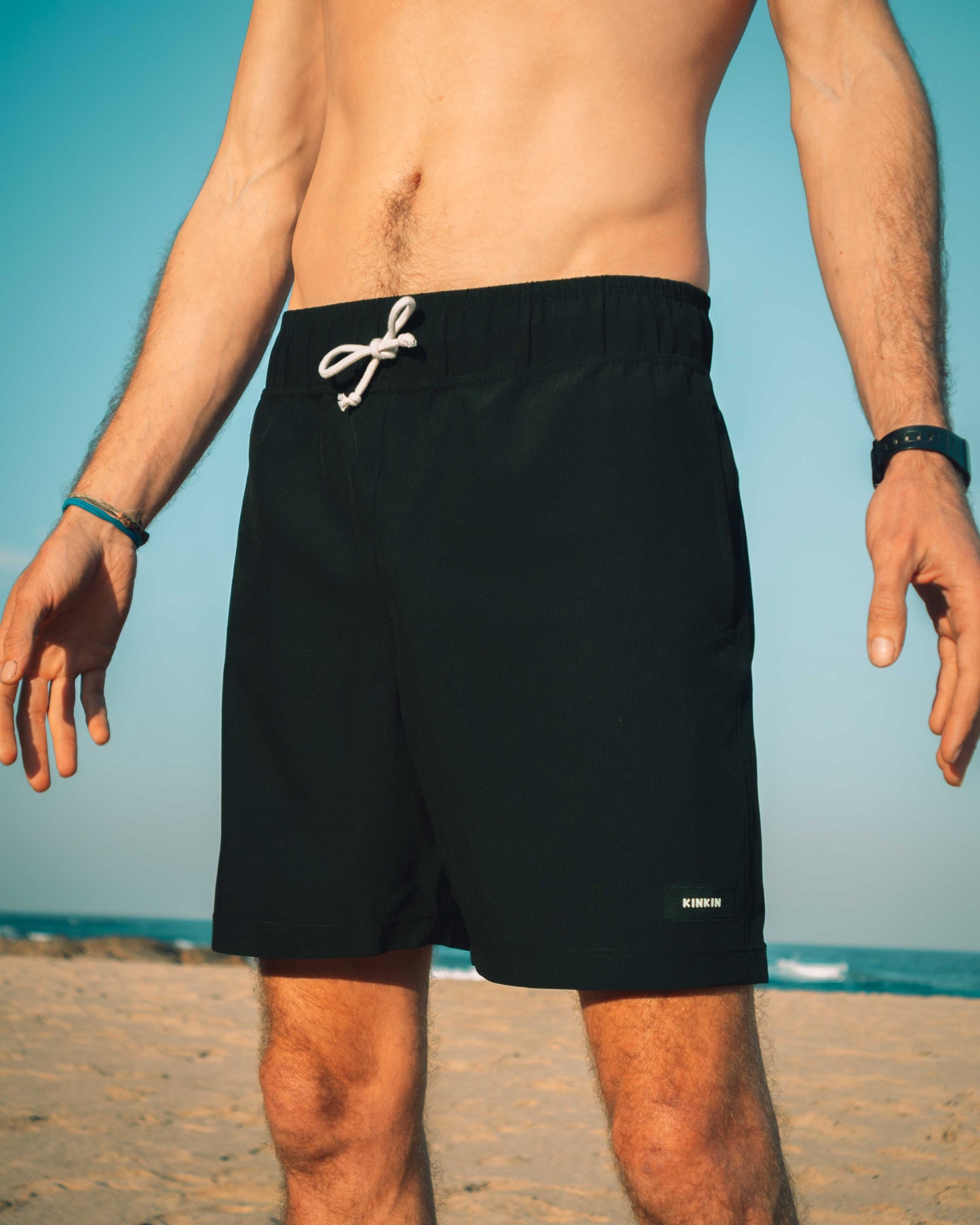 Person wearing black swim shorts with a white drawstring on a beach.
