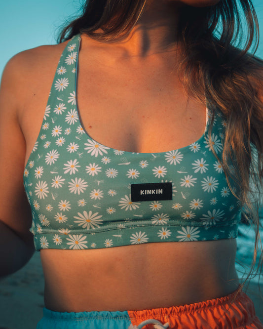 Person wearing a green floral sports bra with 'KINKIN' brand logo against a blue background