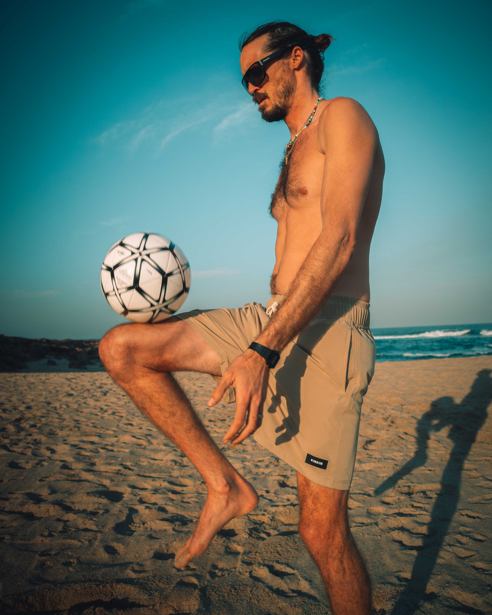 Man playing with a soccer ball on a beach. Wearing khaki swim shorts