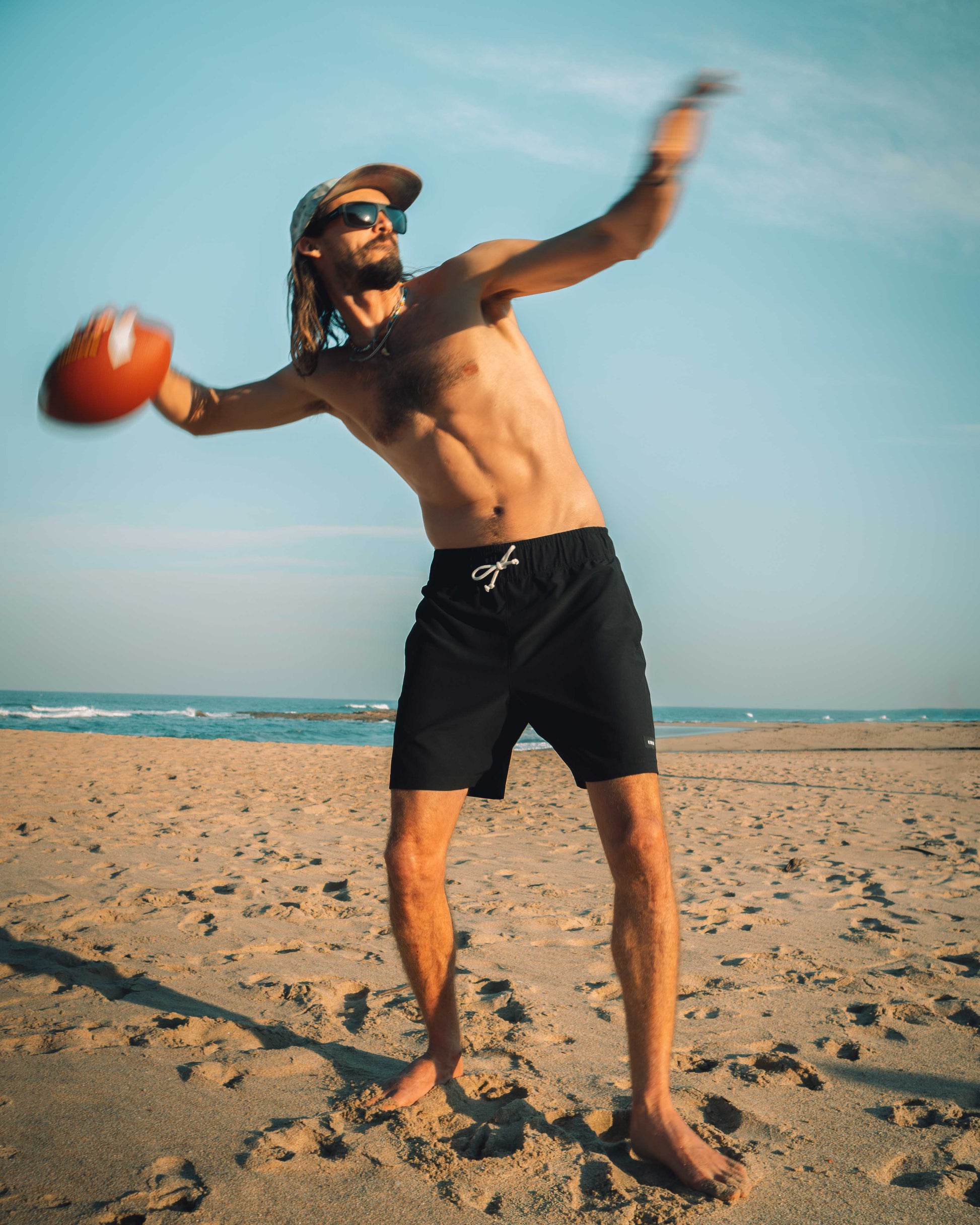 Man playing with a football on a sandy beach, wearing black shorts