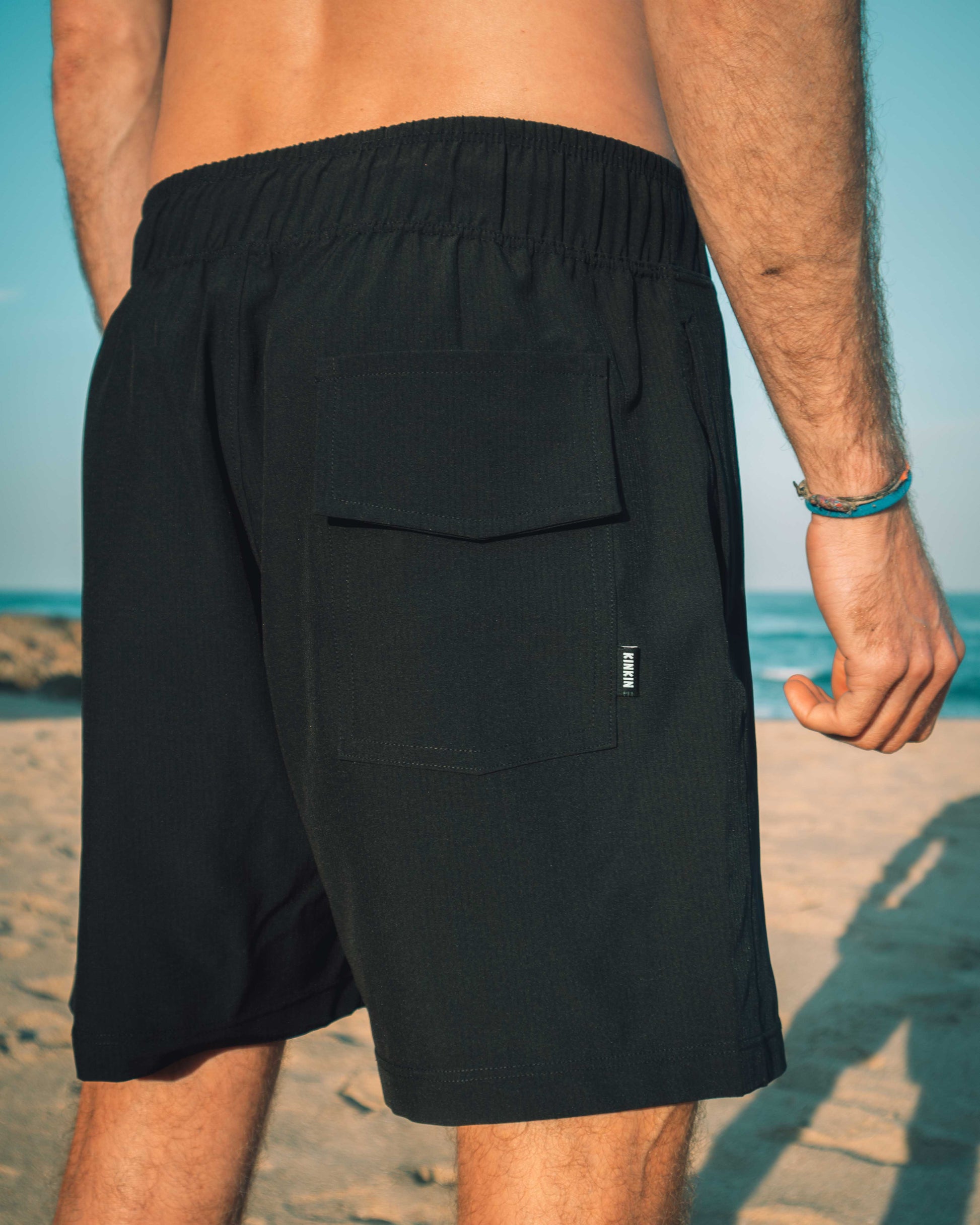Person wearing black shorts on a beach with a clear sky.