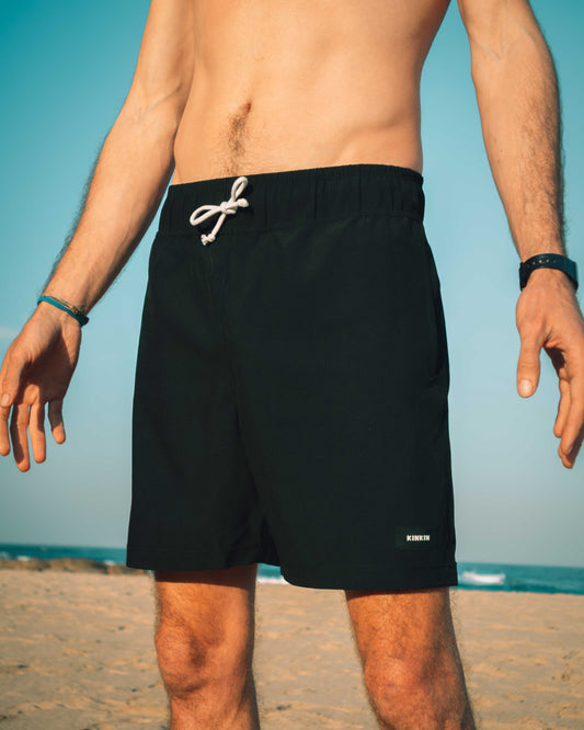 Person wearing black swim shorts with a white drawstring on a beach.