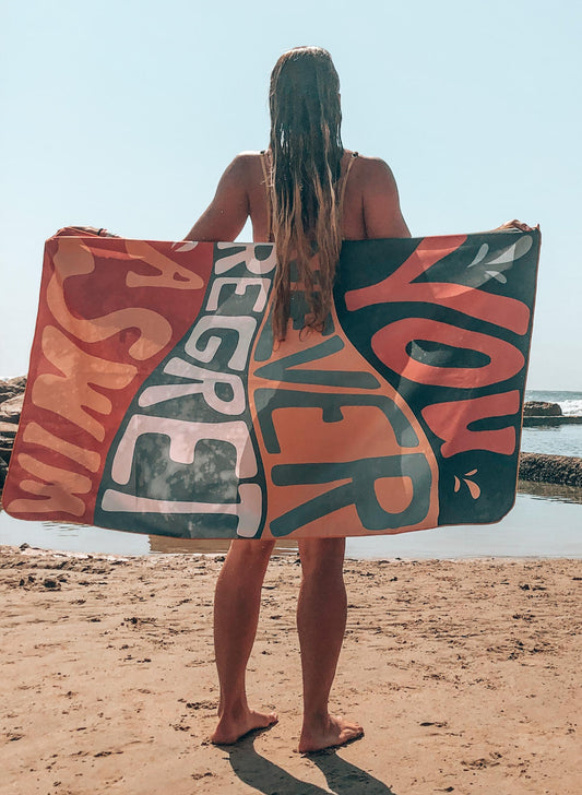 A person standing on a beach holding a checkered red and black towel behind their back.